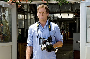 man in blue dress shirt carrying DSLR camera outside the house